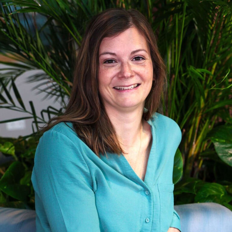Werkende vrouw op kantoor met groene planten achtergrond, professionele headshot, informatief, business, glimlach, vrouw in turquoise blouse.