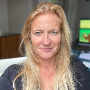 Een professionele vrouw met lange blonde haren in een kantooromgeving, met een computer op de achtergrond, geschikt voor zakelijk en HR-gerelateerd beeldgebruik.