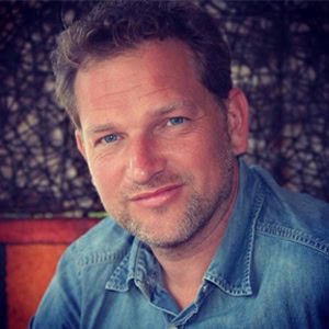 Een professioneel portretfoto van een man met een blauwe denim jas, genomen in een natuurlijke omgeving, geschikt voor persoonlijke en zakelijke doeleinden.