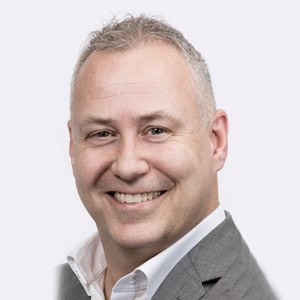 Professionele portretfoto van een lachende man in een lichtgrijs business pak, geschikt voor zakelijke en professionele doeleinden.