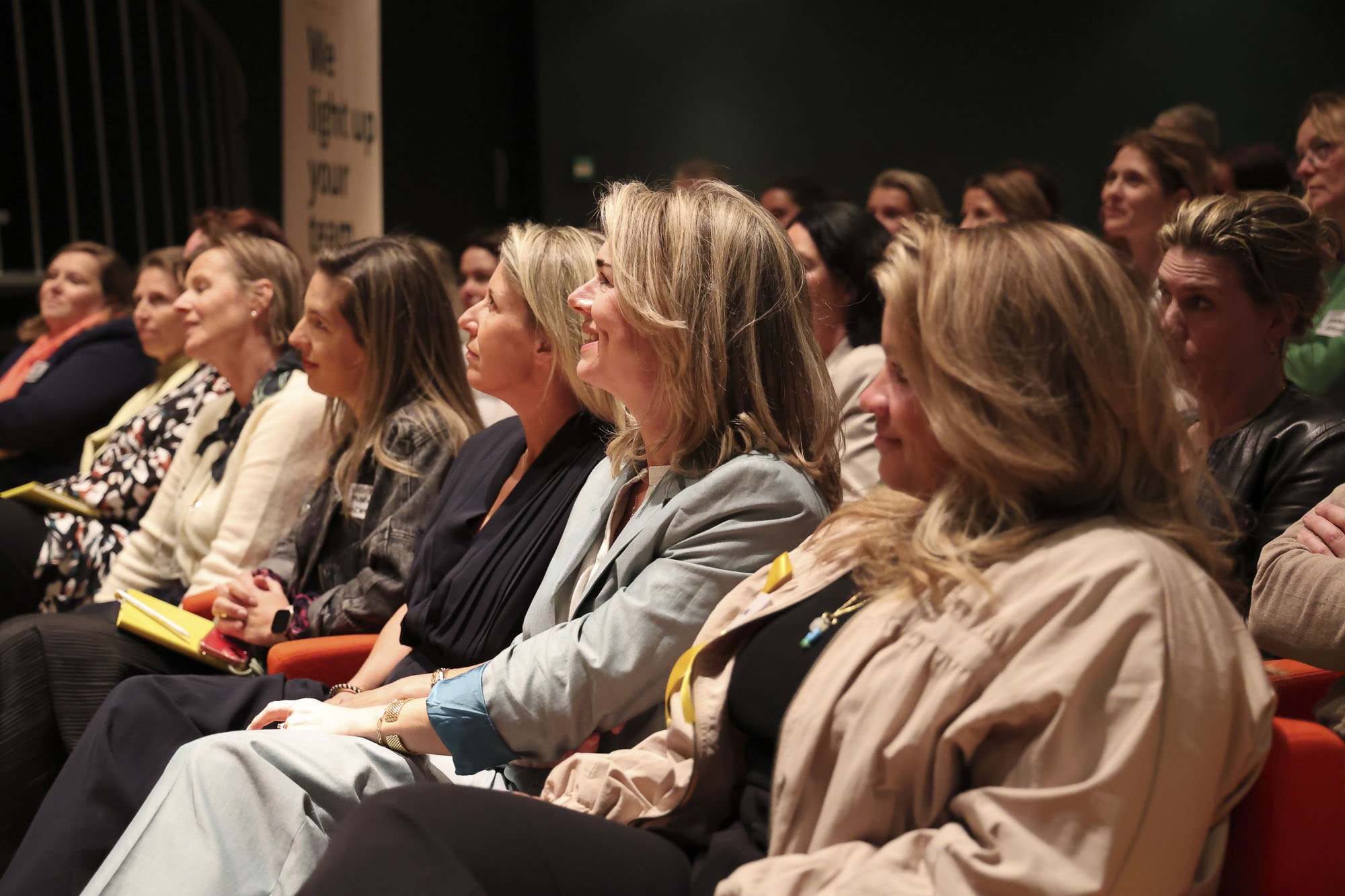 Vrouwelijke professionals zitten samen in een goed verlichte, inspirerende conferentie of seminar, genietend van de presentaties en netwerkmomenten, met aandacht voor leiderschap en persoonlijke ontwikkeling.