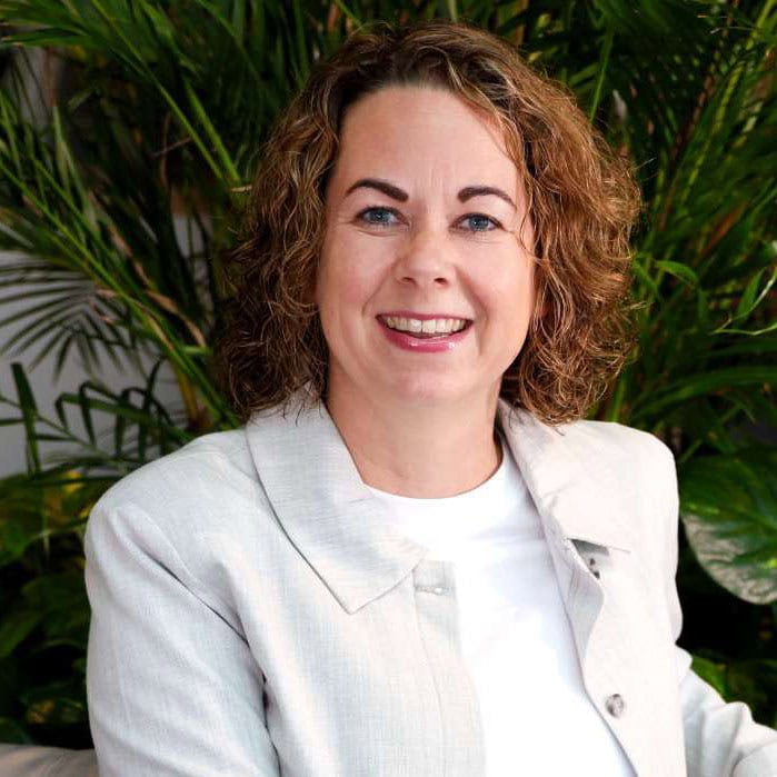 Licht, vrouw met gekruld haar en witte blazer, lachend voor groene planten, moderne en professionele uitstraling, sfeer van positiviteit en energie, stijlvol en natuurlijk, geschikt voor bedrijfs- en lifestylefoto's.