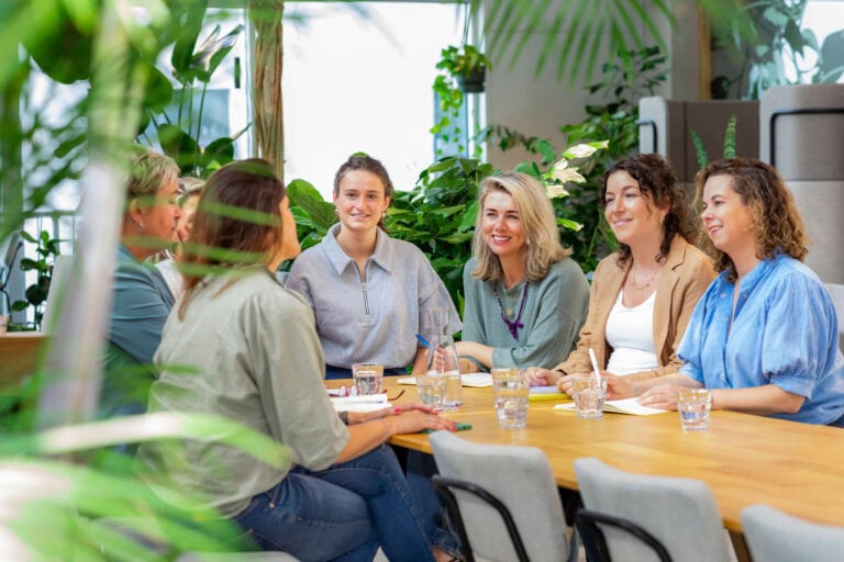 Overleg met een diverse groep vrouwen in een groene, botanische kantooromgeving voor duurzame en creatieve samenwerkingsprojecten.