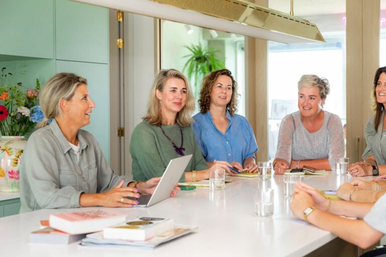 Gezellige zakelijke vergaderingen met vrouwen in een moderne, lichte keukenruimte, gebruikmakend van laptops, notitieboeken en glazen water voor een productieve en inspirerende werksessie.