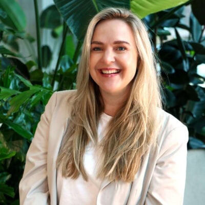 Vrouw met lange blonde haren lachend in groene plantenkas, professioneel en inspirerend, focus op natuur en interieurdesign, enhanceert de SEO met keywords zoals 'groen', 'luxe' en 'binnenruimte'.