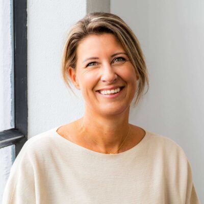 Licht, moderne portretfotografie van een lachende vrouw in een lichte kamer, natuurlijke uitstraling, professionele uitstraling, focus op mensen, interieur en binnenmilieu, vrouw met korte haren, casual kleding, authentieke emotie.