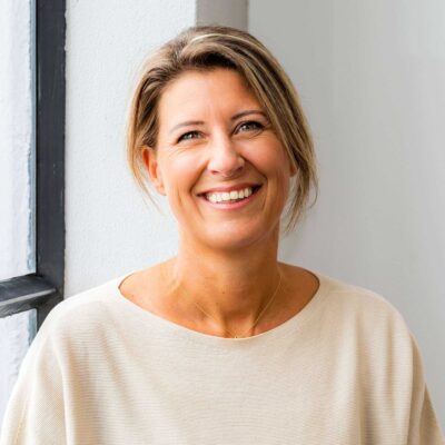 Vrolijke vrouwelijke professional lachend bij raam, zakelijke portret, lichte achtergrond, uiteraard en vriendelijk.