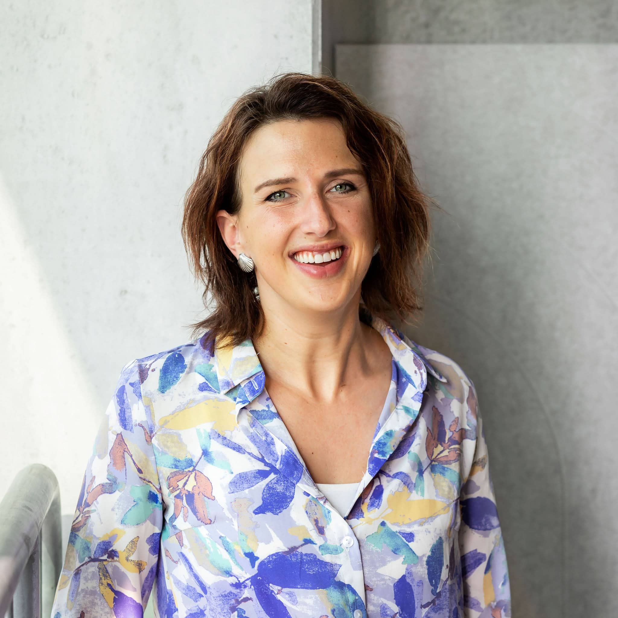 Gladys vrouw in kleurrijke blouse smiling in een moderne omgeving.