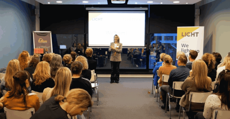 Verlichte spreker tijdens zakelijke presentatie bij LICHT conferentie met publiek in moderne zaal.
