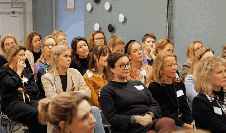 Diverse vrouwen en mannen luisteren aandachtig tijdens een conferentie of seminar, met focus op betrokkenheid, leren en netwerken binnen professionele evenementen.