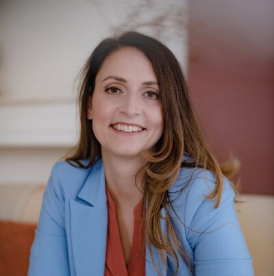 Holdende vrouw in zakelijke blazer met glimlach, professioneel portret, binnen, licht en vriendelijk kader.