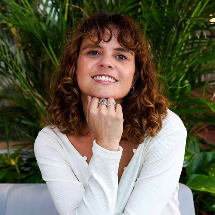 Glimlachende vrouw met curly haar in een witte top die groenten achter zich heeft voor een natuurlijke sfeer licht en frisse uitstraling.