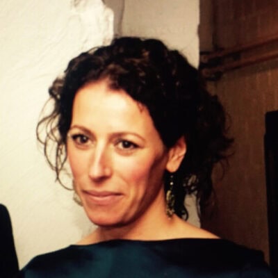 Gezicht van een vrouw met donkere, krullende haar, sfeervolle binnenverlichting, artistieke portret voor LICHT en interieurverlichting, natuurlijke uitstraling, creatieve lichtcombinatie.