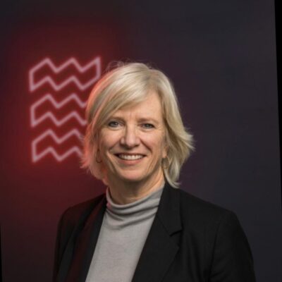 Heldere lichtkunstfotografie van een lachende vrouw met blonde haar, gekleed in een zakelijke outfit, tegen een donkere achtergrond met neon lichtpatroon, geschikt voor moderne kunst en creativiteit.