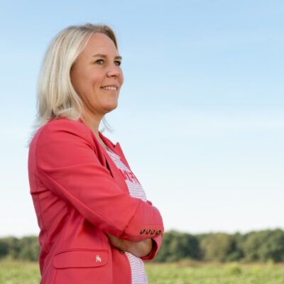 Schermafbeelding van een vrouw die trots de vrije natuur bewondert onder een heldere, blauwe lucht, symboliseert rust, inspiratie en welzijn.