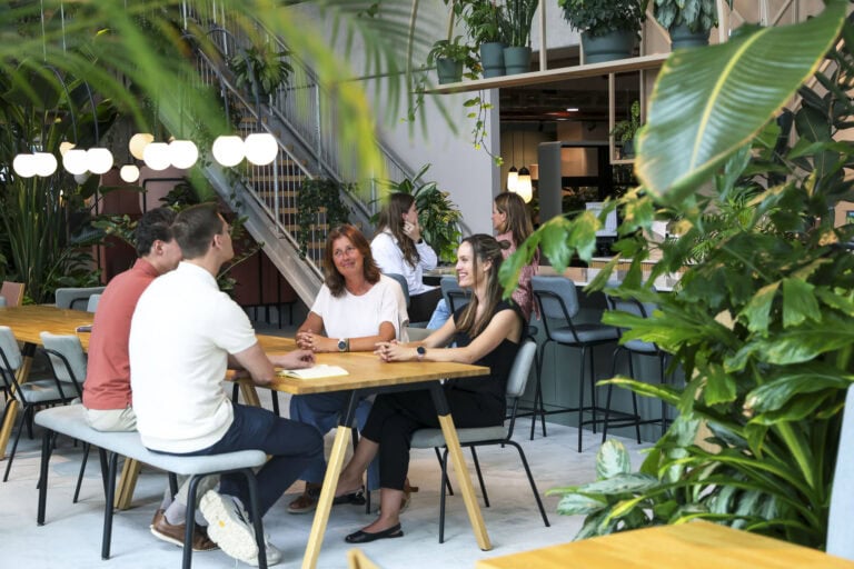 Gezellige groep mensen in een modern kantoor met groene planten en natuurlijke verlichting, creëren een comfortabele en inspirerende werkomgeving.