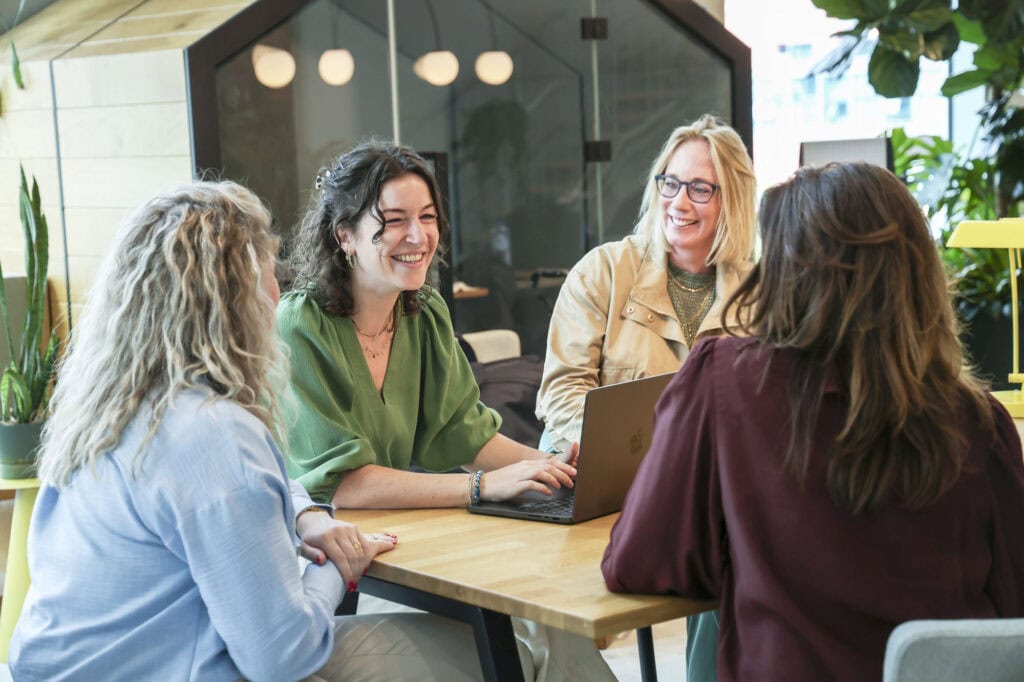 Vriendelijke vrouwen werken samen in een lichte, moderne kantoorruimte met groene planten voor een inspirerende werkomgeving.