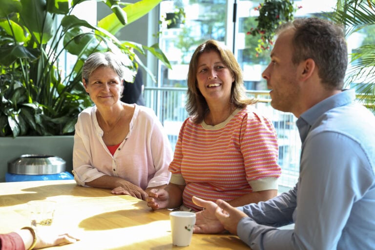 Gezellige groepsgesprek in een licht interieur met veel groen, warme sfeer en natuurlijk daglicht, ideaal voor sfeerbeschrijving en foto’s over communicatie en samenwerking.