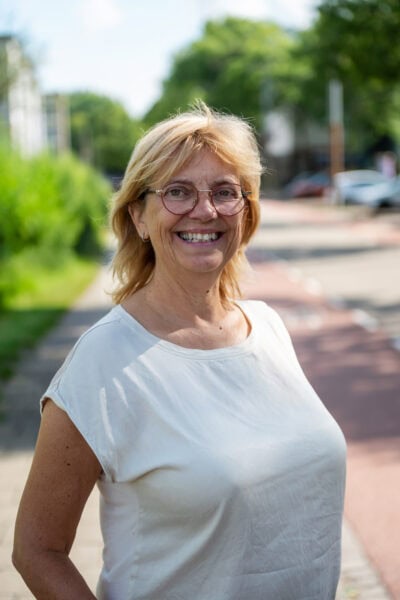 Vrolijke oudere vrouw met glazen, lachend op straat in de zonnige buitenlucht, genietend van het mooie weer en positieve sfeer.