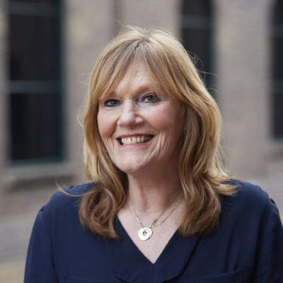LICHT, portretfoto van een lachende vrouw met rood haar en blauwe ogen, professionele uitstraling, buitenportret met stedelijke achtergrond, geschikt voor zakelijke en persoonlijke doeleinden, authentiek en warm beeldo.