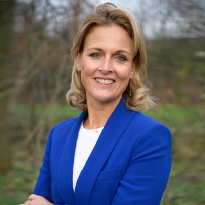 LICHT, professionele portretfoto van een zelfverzekerde vrouw in een blauwe blazer, buiten in een natuurlijke omgeving met bomen, geschikt voor zakelijke en persoonlijke branding.