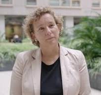 Onbekende vrouw die nadenkt in een groene buitenomgeving met gebouwen op de achtergrond.
