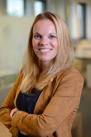 Gezicht van een lachende vrouw met lang haar, professioneel in een moderne kantooromgeving, gericht op zakelijke en persoonlijke groei.
